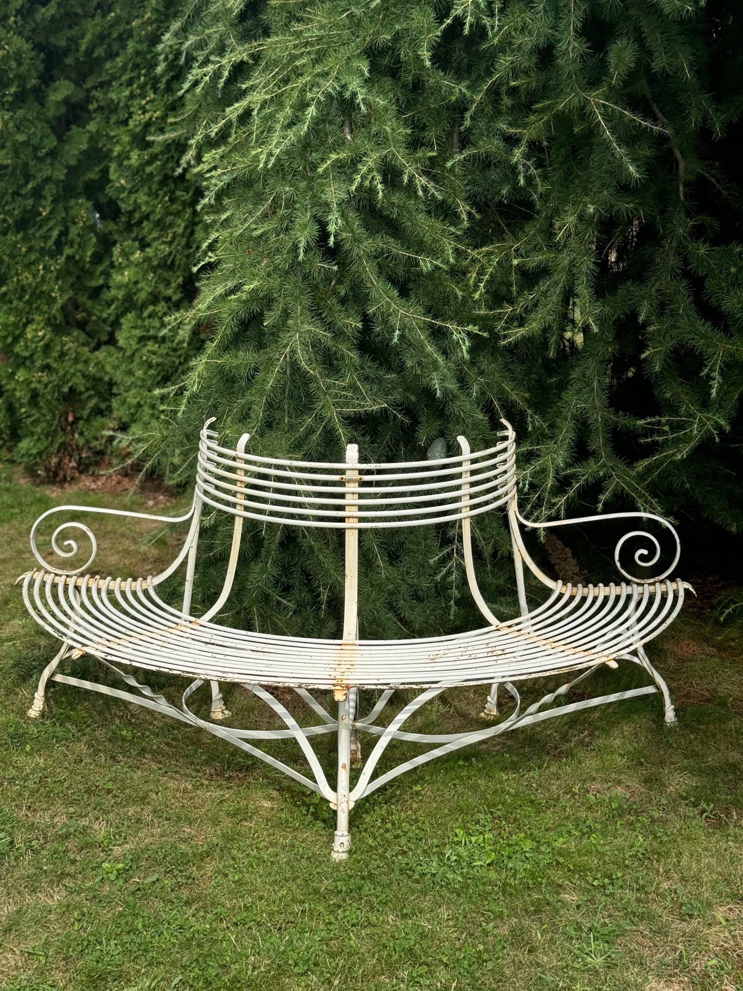Decorative white metal bench in a garden setting with green trees in the background
