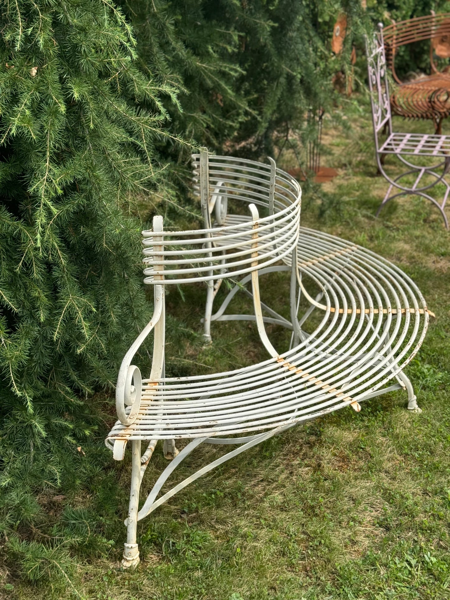 Wrought iron garden bench in a garden setting with trees and grass.