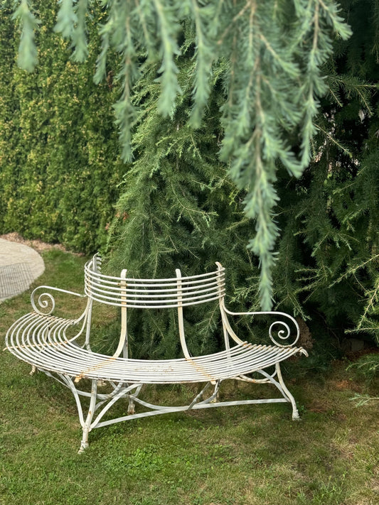 White metal bench in a garden setting with trees and grass.