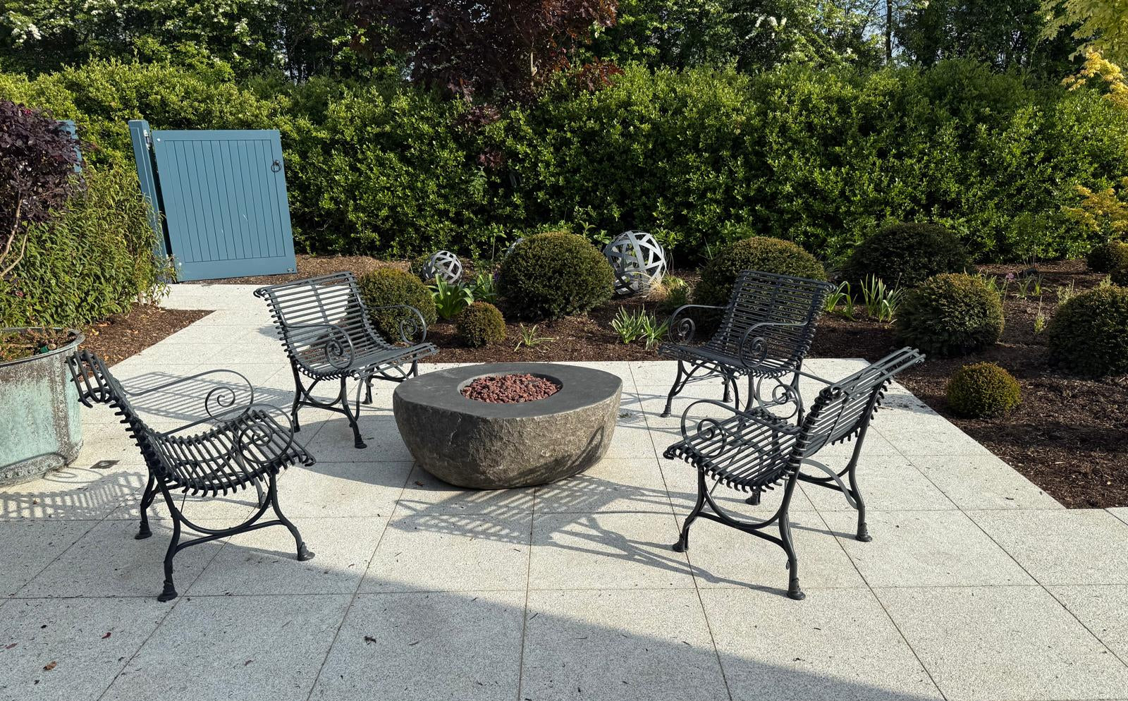 Outdoor patio with a fire pit and chairs surrounded by greenery