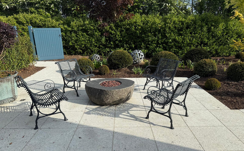 Outdoor patio with a fire pit and chairs surrounded by greenery